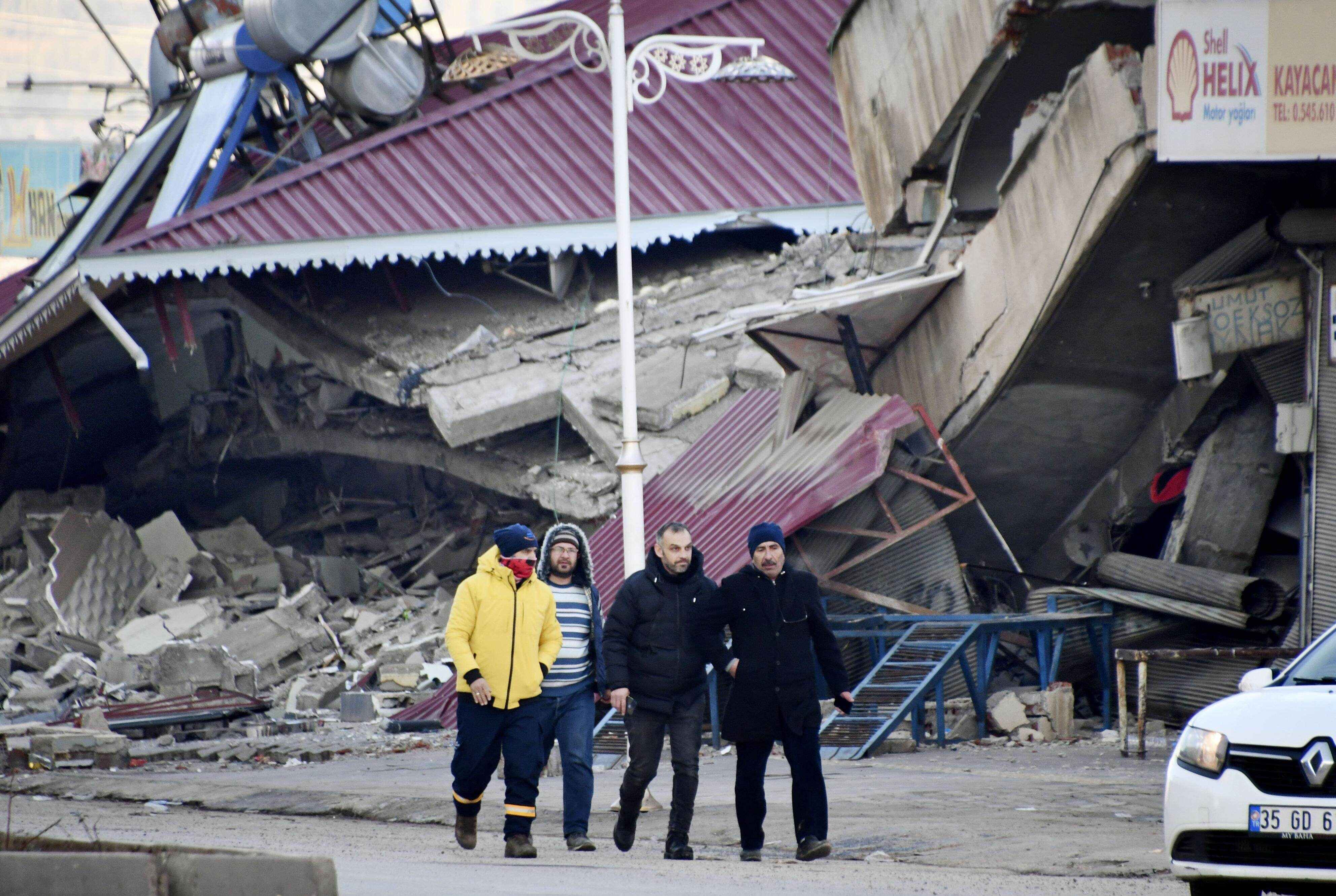 People walk in front of collapsed buildings in Pazarcik in Turkey’s southern province of Kahramanmaras on February 8, 2023, after a powerful earthquake hit the nation and neighboring Syria. Photo: Kyodo