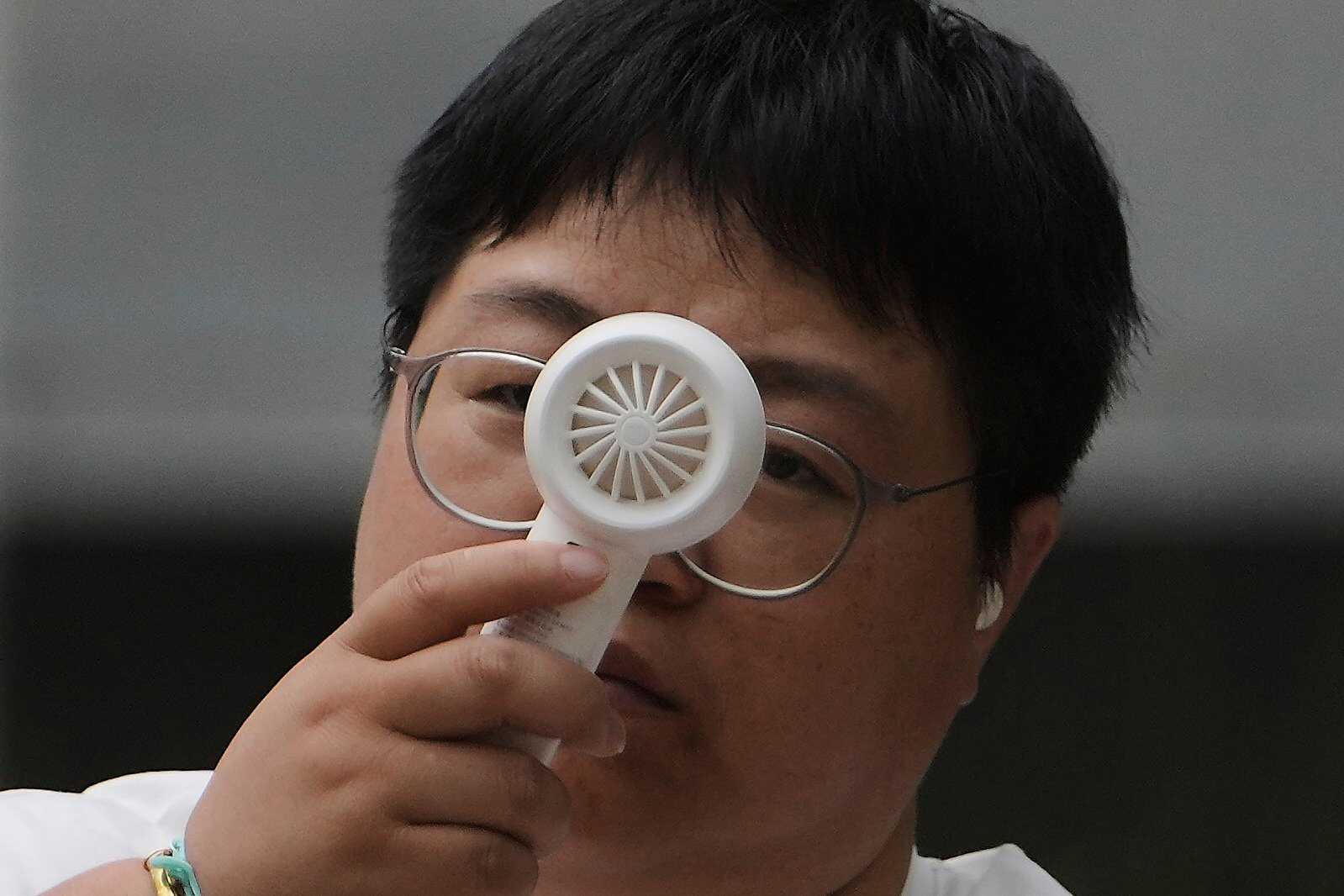 A woman cools herself with a portable electric fan as she rests on a bench on a sweltering day in Beijing. Photo: AP