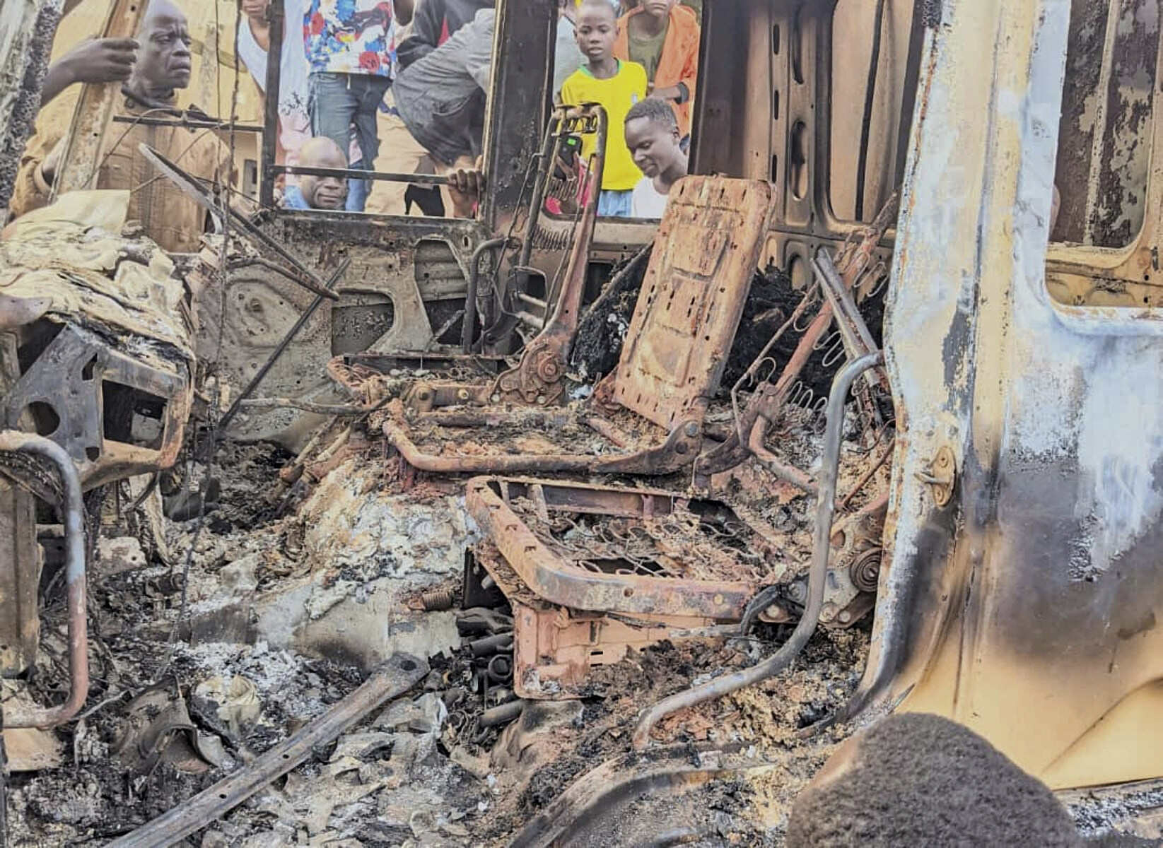 People gather around the charred remains of a vehicle burned during a deadly attack and massacre in Komanda, Ituri province in northeastern Democratic Republic of Congo, Sunday, July 27. Photo: AP
