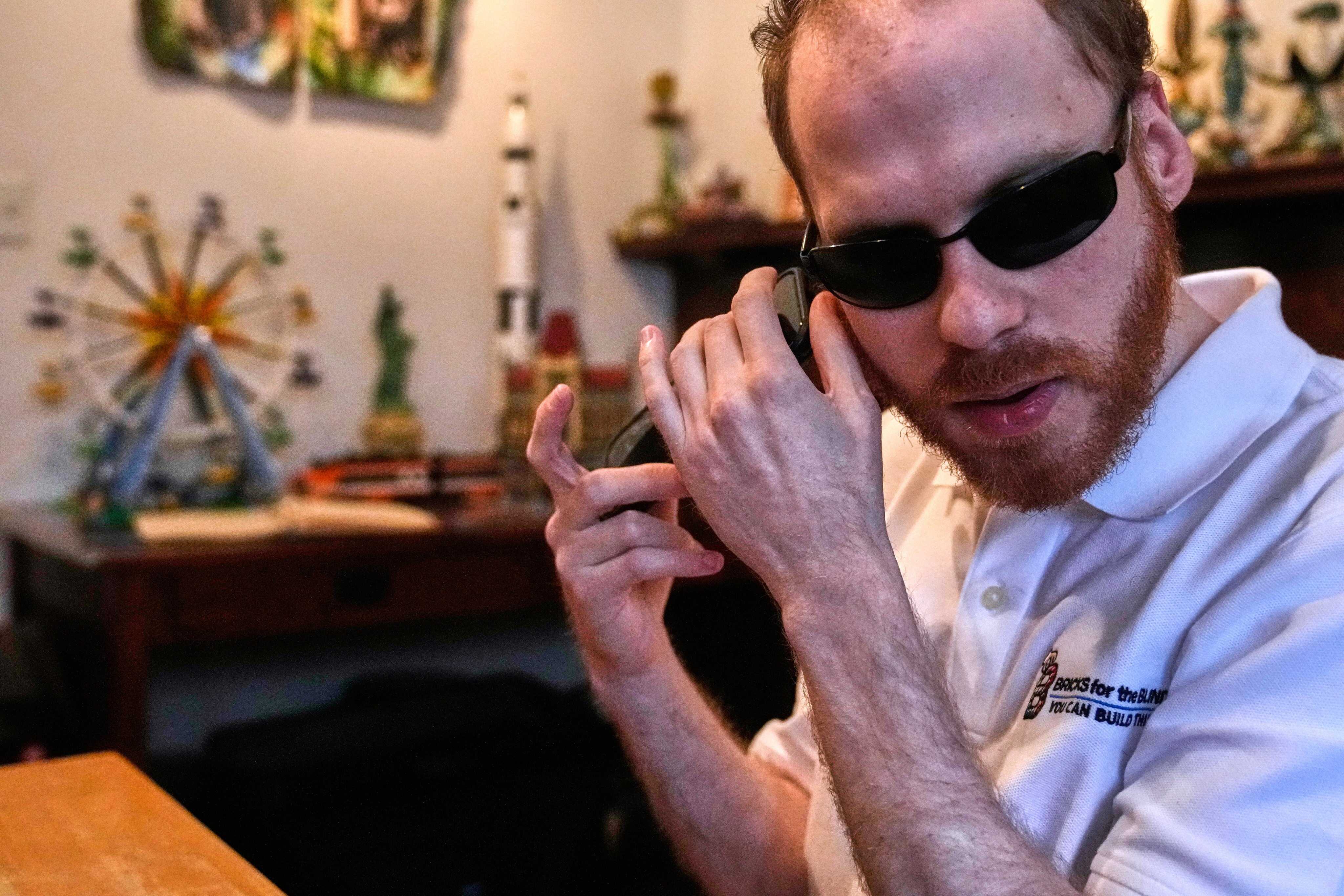Matthew Shifrin, the founder of Bricks for the Blind, listens to directions on his phone while building a LEGO gum ball machine at his family’s home. Photo: AP