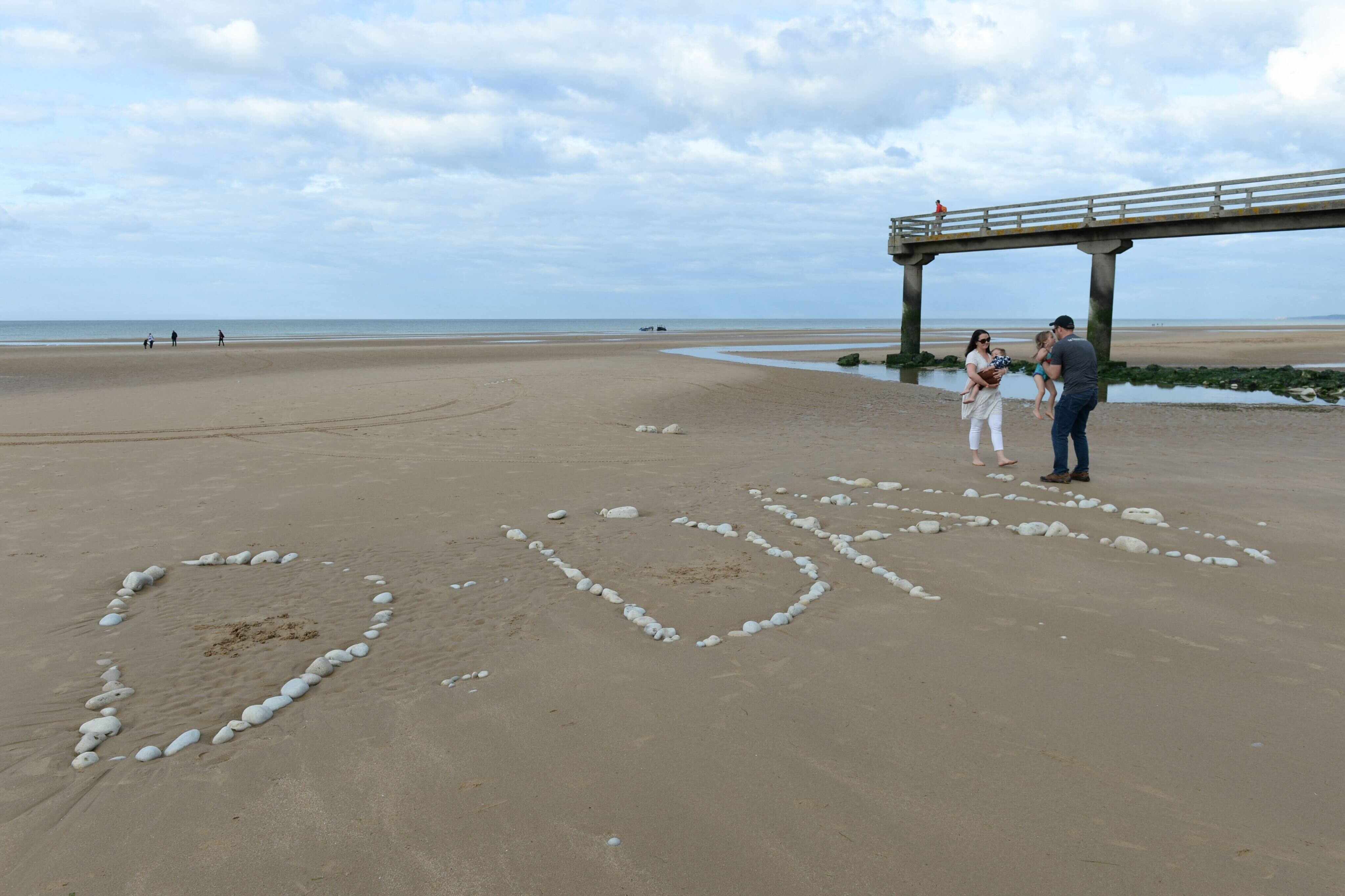 A family stands next to the word “D-Day” written with stones on “Omaha Beach” in Vierville-sur-Mer, northwestern France. Photo: AFP