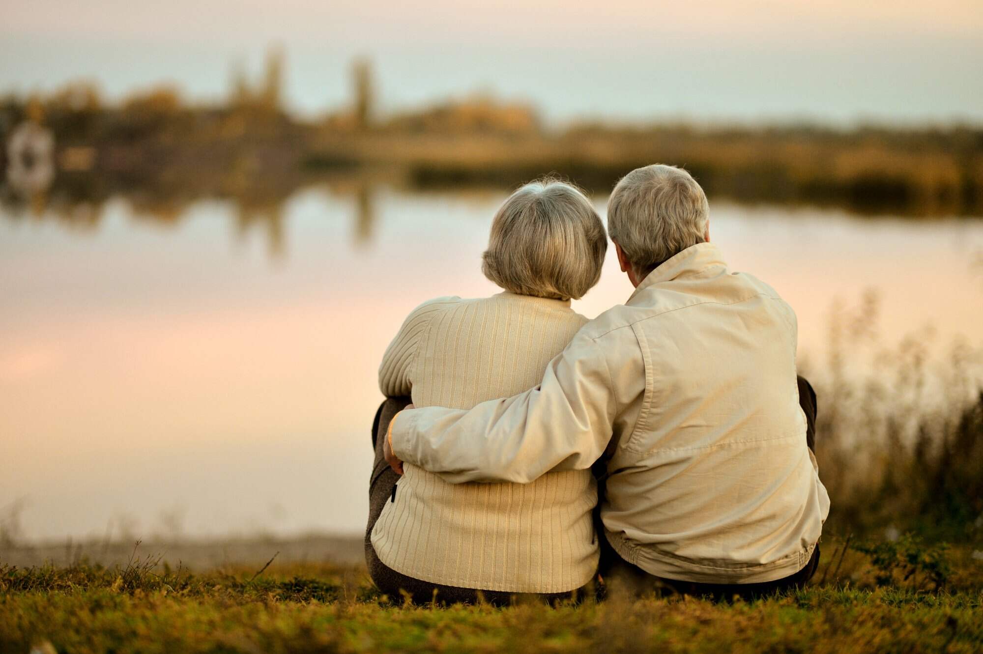 Happy senior couple sitting in summer near lake during sunset