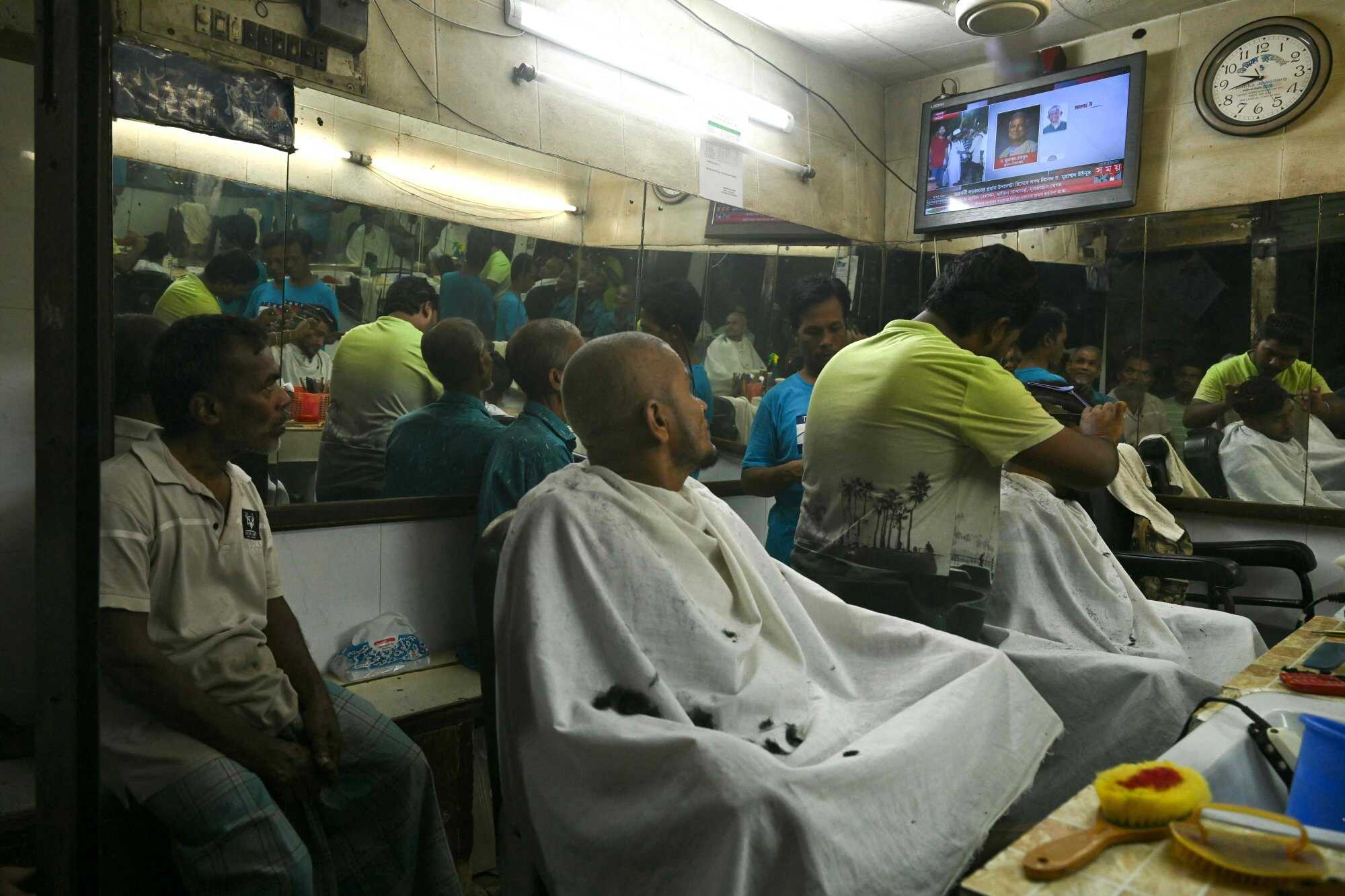 Customers at a barber shop in Dhaka watch on television the swearing in of economist Muhammad Yunus. Photo: AFP