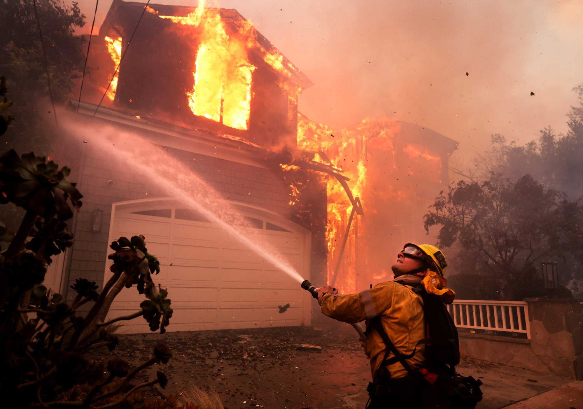 Firefighters battle a house fire off Bollinger Drive in Pacific Palisades, California, United States after a brush fire spread quickly with heavy winds on January 7. Photo: Los Angeles Times/TNS