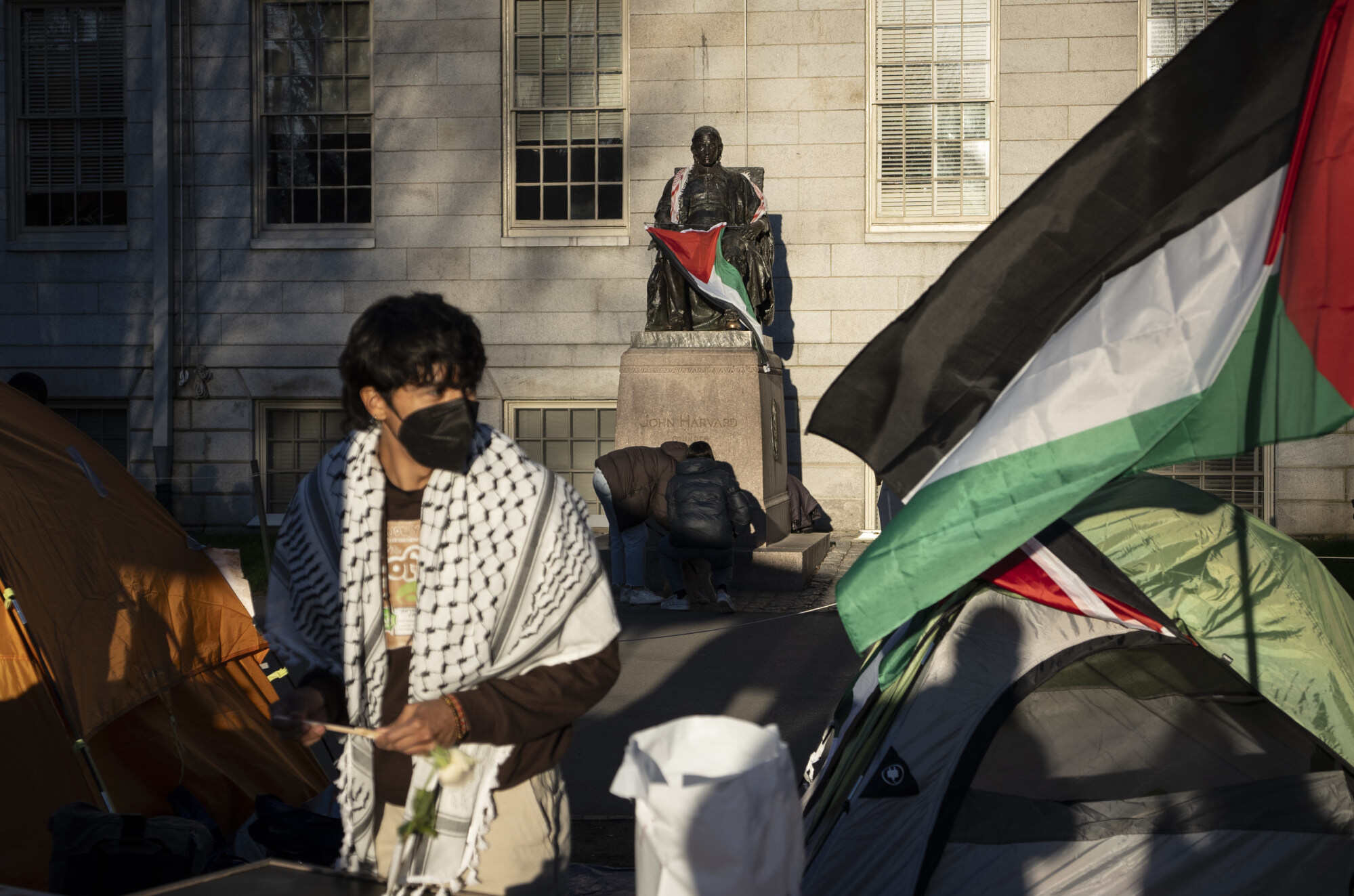 A demonstrator stands in front of the statue of John Harvard – the first major benefactor of Harvard College – draped in the Palestinian flag at a student encampment protesting against the war in Gaza in April 2024. Photo: AP