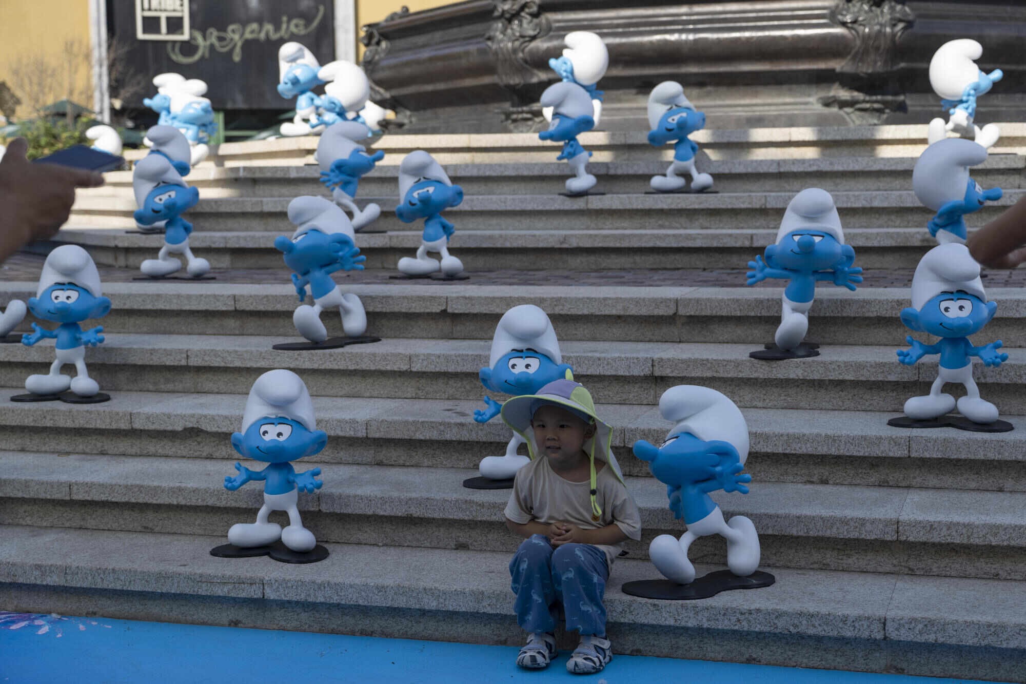 A child sits with life-size blue figures – characters from the ‘Smurf’ film – in Beijing, China. Photo: AP