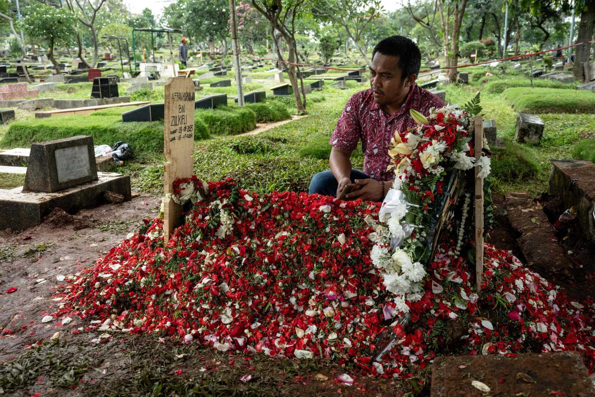A friend at the flower-covered grave of Affan Kurniawan, the 21-year-old motorcycle driver who was killed after being run over by a police vehicle. Photo: AFP