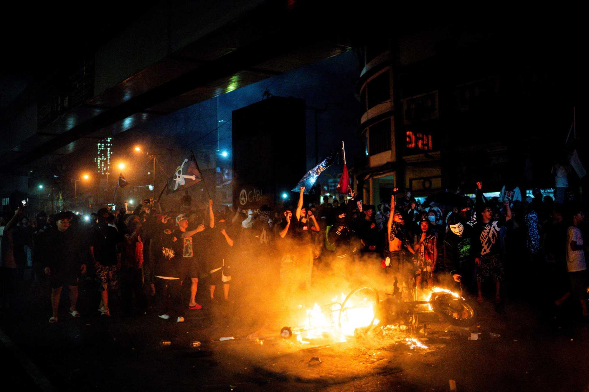 Demonstrators with flags stand next to a burning motorcycle during a protest against corruption linked to flood control projects in Manila, Philippines. Photo: Reuters