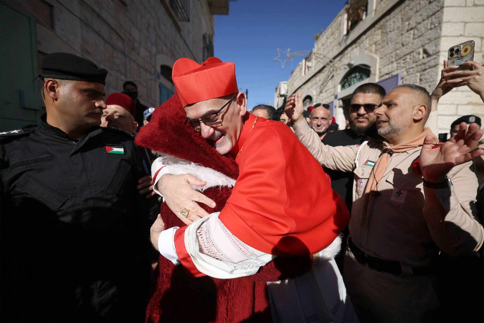 The Latin Patriarch of Jerusalem, Cardinal Pierbattista Pizzaballa, hugs a man dressed as Santa Claus as he is welcomed by pilgrims, tourists and Palestinians upon arrival to lead Christmas Mass in the Church of the Nativity in the Israeli-occupied West Bank city of Bethlehem. Photo: AFP