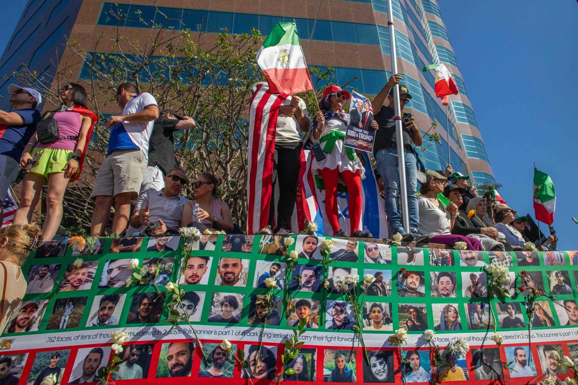 Iranians in the United States hold flags by a wall with a sign with pictures of people who died in January’s anti-government protests in Tehran, while celebrating the US-Israel strikes and the death of Khamenei. Photo: AFP