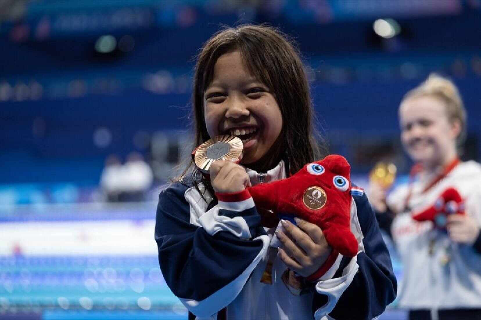 Jasmine Ng bites her bronze medal after the women’s SB6 100m breaststroke final at the Paris Paralympics. The 14-year-old became the youngest athlete and medallist to represent the city at the Paralympics. Photo: China Hong Kong Paralympic Committee.