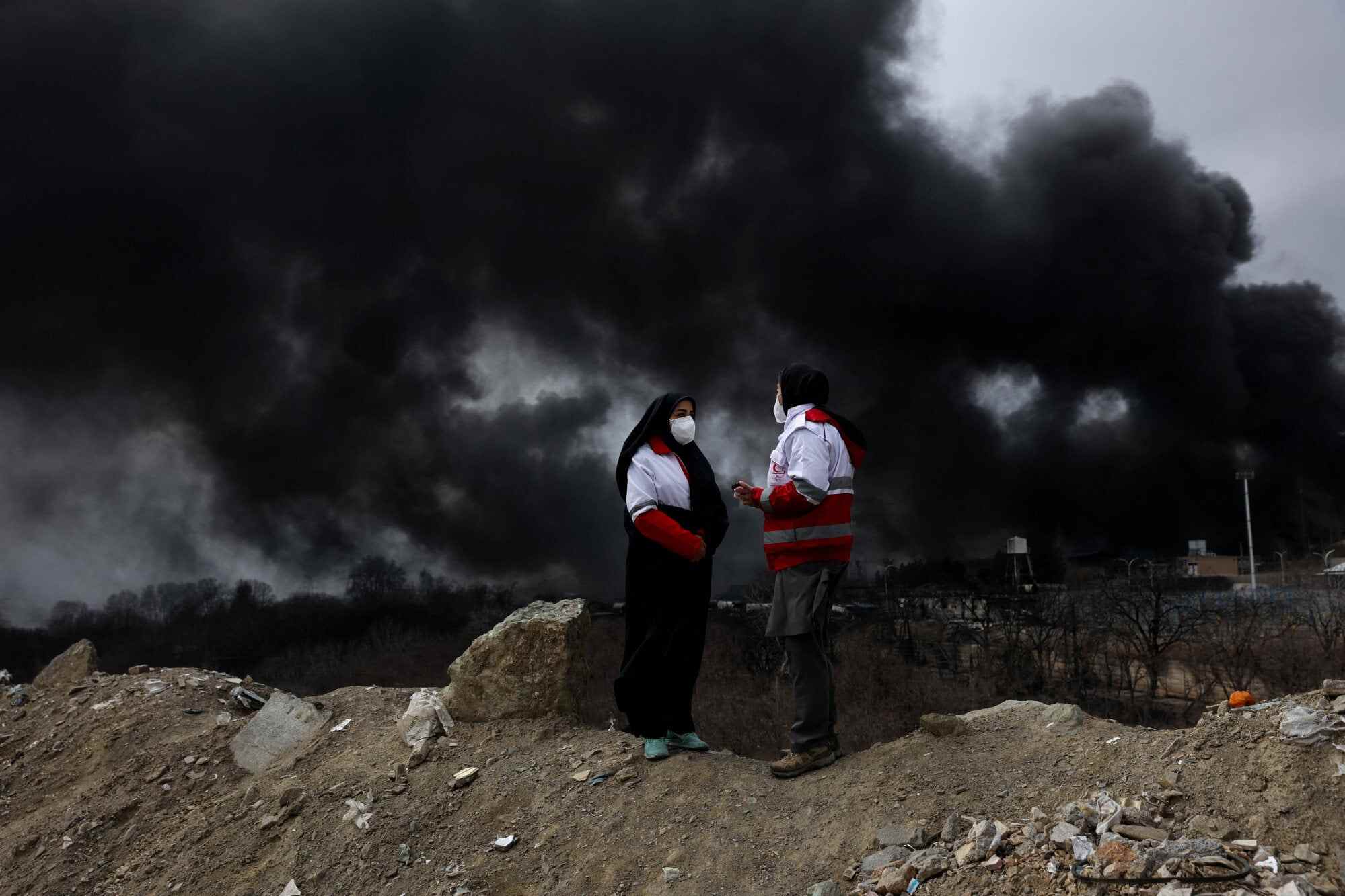 Members of the Red Crescent talk to each other as smoke rises after a reported strike on Shahran fuel tanks, amid the US-Israeli war on Iran, in Tehran. Photo: Reuters