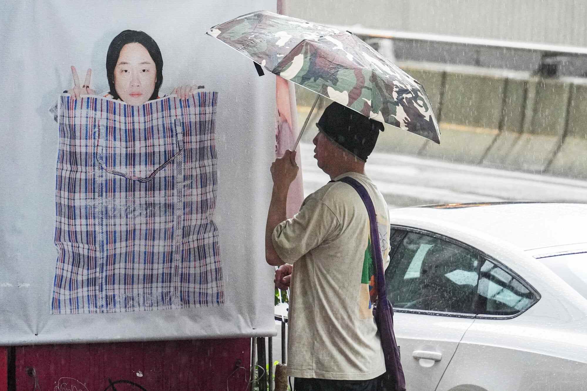 A man holds an umbrella in front of a Jimmy O. Yang poster in Central. Photo: Eugene Lee