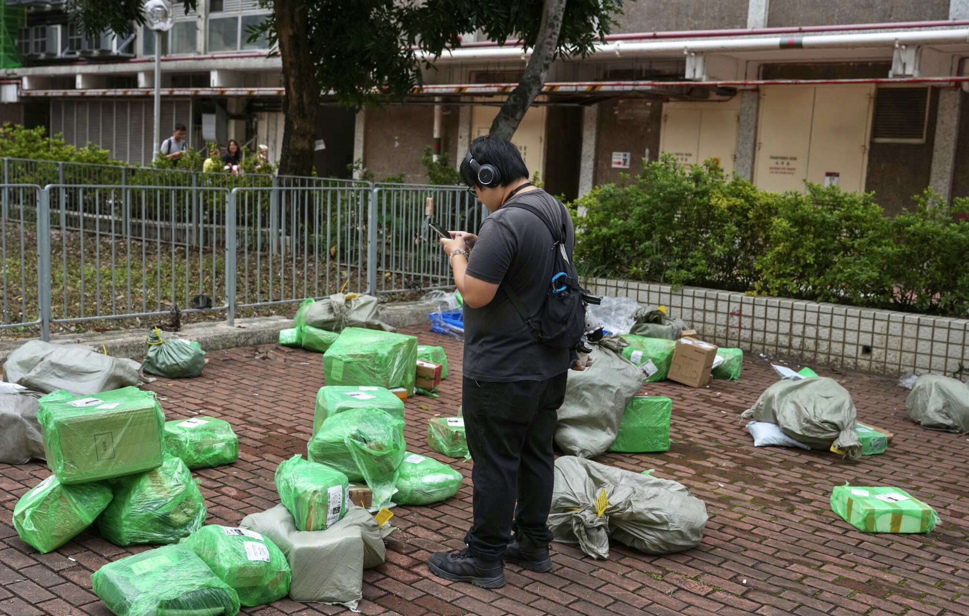 A man checks his phone while standing among parcels wrapped in green plastic and sacks at Lai Kok Estate in Cheung Sha Wan. Photo: Karma Lo