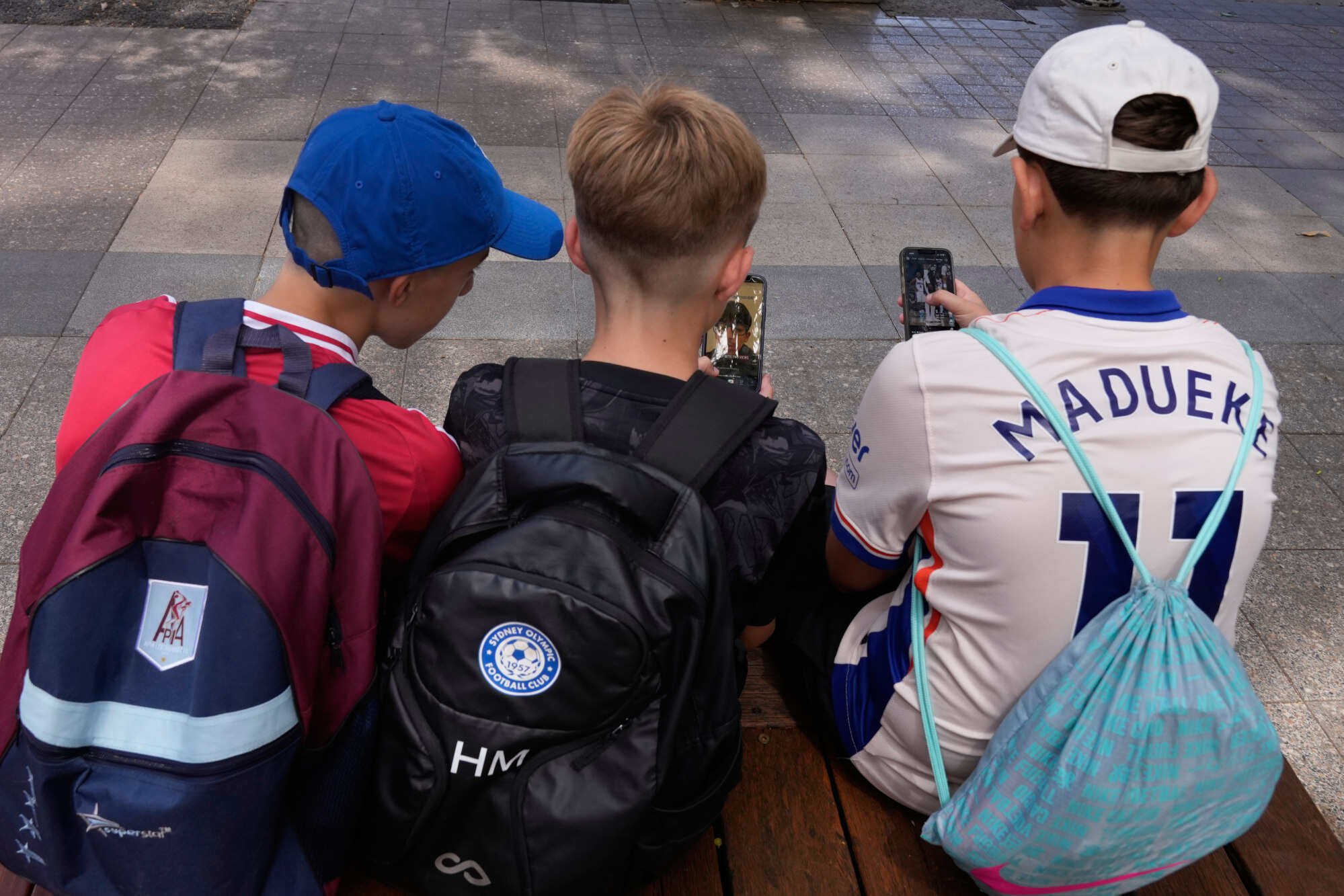 Three boys use their phones while sitting outside a school in Sydney. There are still too many children on social media, Albanese said in a statement. Photo: AP