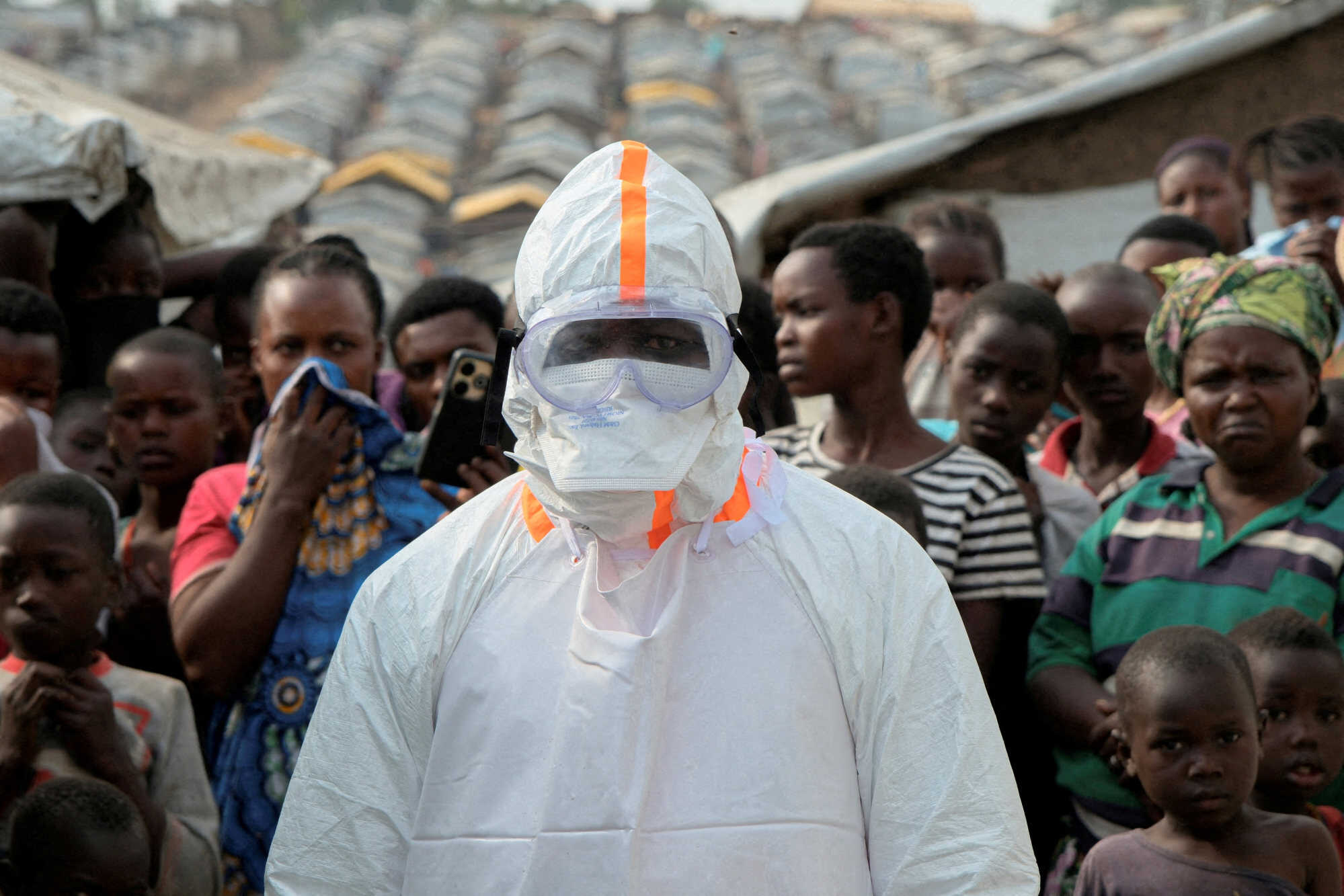 A health worker in personal protective equipment stands near displaced people waiting for the burial of suspected Ebola victims at the Kigonze displaced persons camp, one month after an outbreak was declared, in Bunia in June. Photo: Reuters