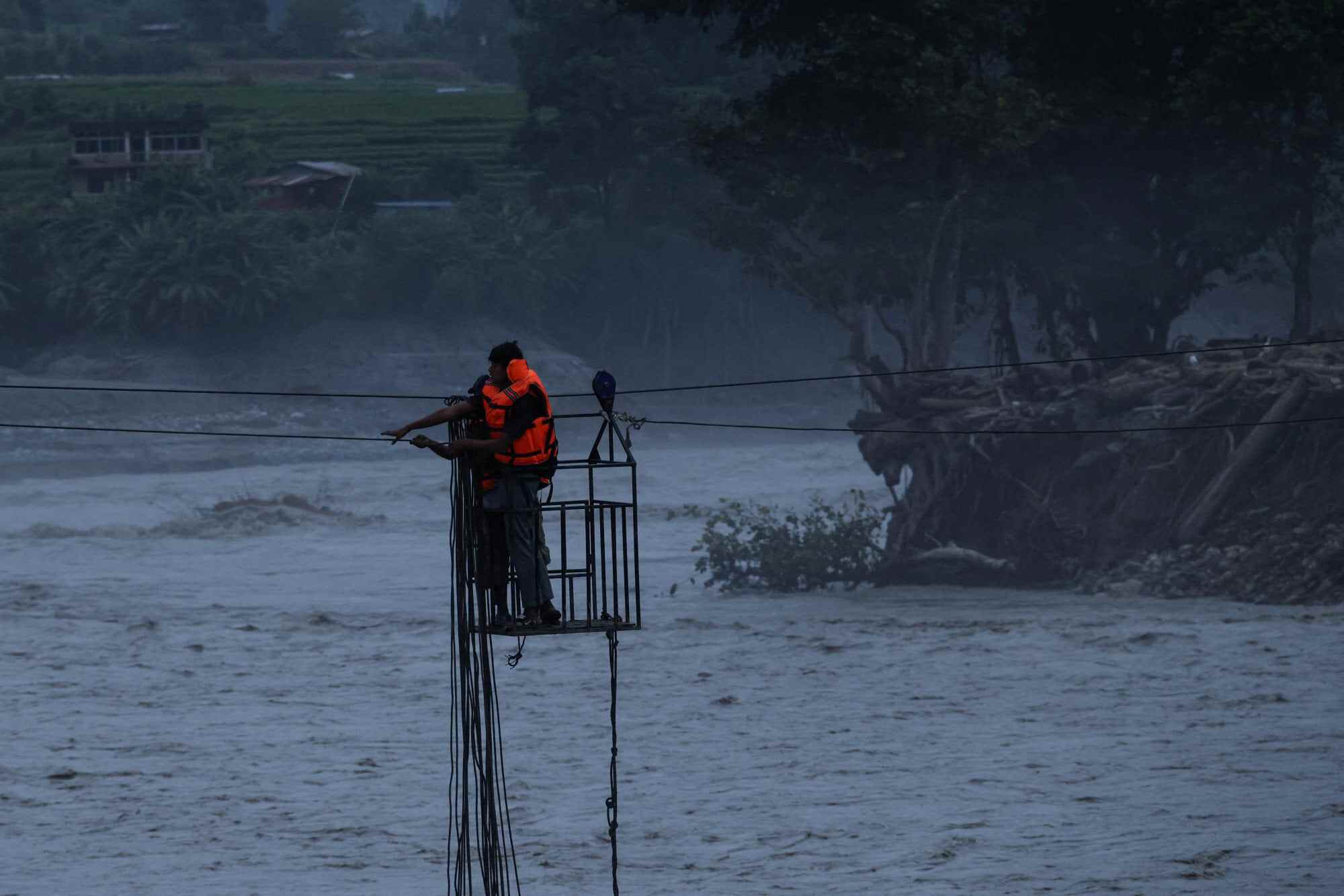 People hold onto a wire cage on a makeshift zip line as they cross the Trishuli River following deadly flash floods and a mudslide that damaged bridges and stranded residents in Devighat, Nuwakot district, Nepal. Photo: Reuters