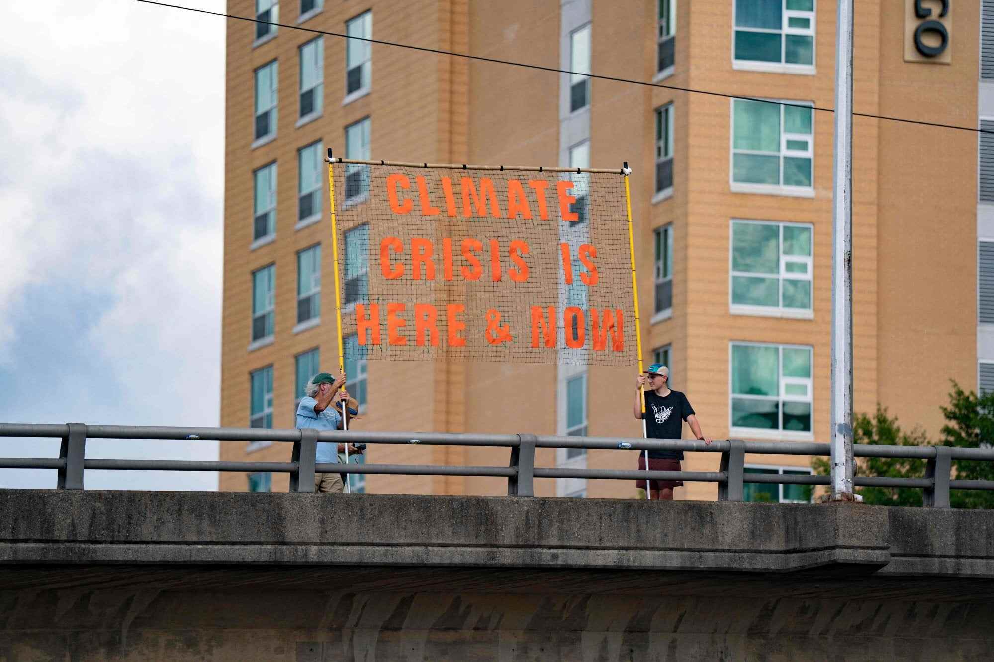 People hold a sign reading “climate crisis is here and now” on an overpass ahead of the G20 finance ministers meeting on August 28, 2026, in Asheville, North Carolina. Photo: AFP